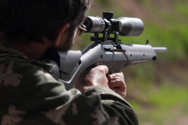 Modern bir tüfek tutan adam bir hedef vurmaya hazırlanıyor