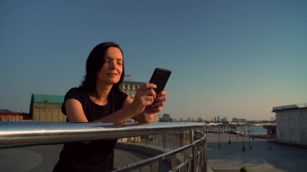 Menina está em pé perto da cerca e digitar uma mensagem — Vídeo de Stock