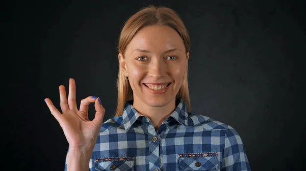 肖像年轻的白种女人 金色的头发摆在黑色的背景 迷人的女孩穿着休闲明亮的衬衫看着与友好的微笑显示手势 的相机 — 图库照片