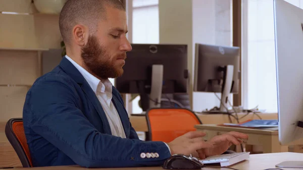 Knappe Kaukasische Man Met Baard Zit Aan Werkruimte Typen Het — Stockfoto