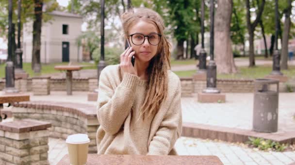 Lachende hipster meisje praten door mobile in park — Stockvideo