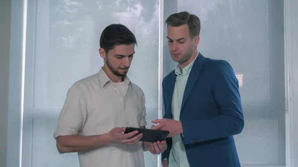 Young casual worker holding touch screen tablet. Adult caucasian man wearing in blue suit.