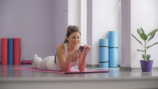 Girl lying on the yoga mat and looking at the phone.