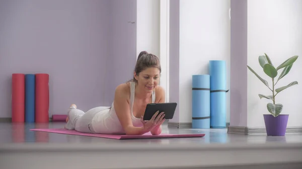 Mujer acostada en una esterilla de yoga y mirando la tableta — Foto de Stock