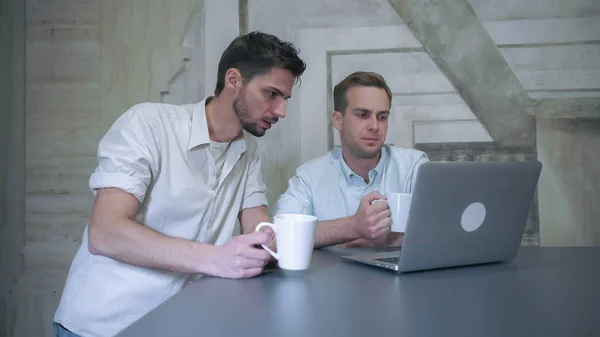 Dwóch młodych mężczyzn profesjonalnych picia kawy wyglądają do komputera i dyskusja — Zdjęcie stockowe