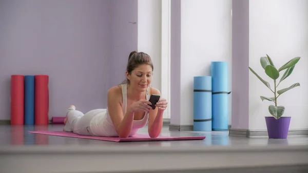 Vrouw liggend op een yoga mat en kijken naar de telefoon — Stockfoto