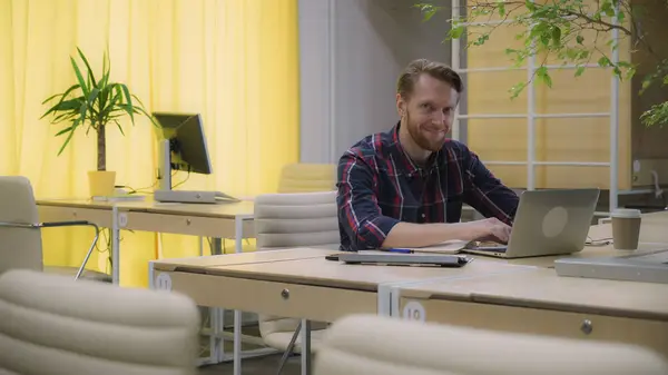 Бородатый человек с концентрацией работает на компьютере, смотрит вверх и улыбается . — стоковое фото