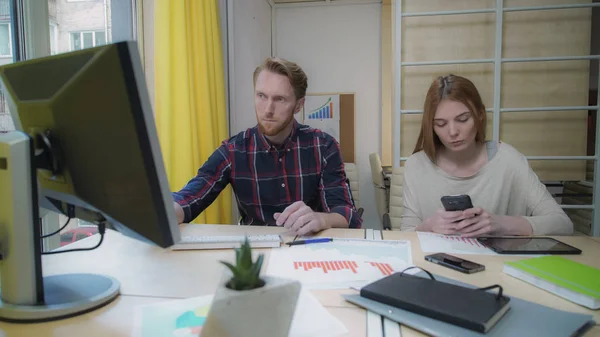Девушка пристально смотрит в смартфон, мужчина, работающий за компьютером . — стоковое фото
