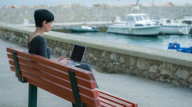 Young woman working on the computer outdoor on the pier. clipart