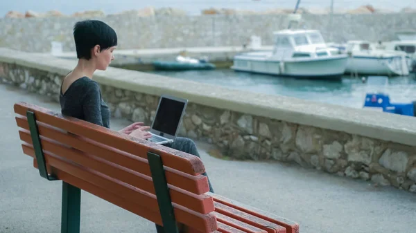 Junge Frau arbeitet draußen auf der Seebrücke am Computer. — Stockfoto