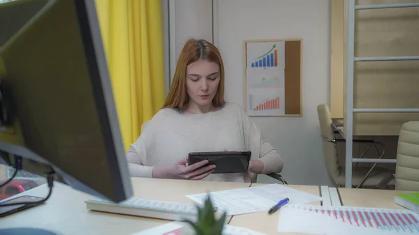 Vrouw zit op de werkplek, in de handen met de tablet. — Stockfoto