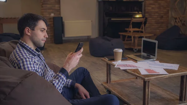 Gestionnaire parlant au téléphone tout en étant assis dans un fauteuil facile, un ordinateur portable est sur la table . — Photo