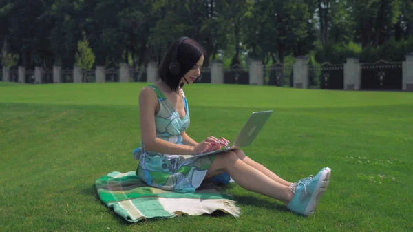 Uma jovem se senta em cobertor e digitando em um laptop ao ar livre — Fotografia de Stock