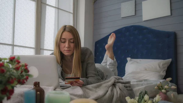 Blond in bed with a laptop spends money.