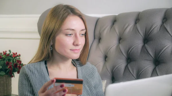 Blonde girl sitting on the couch purchases via the Internet