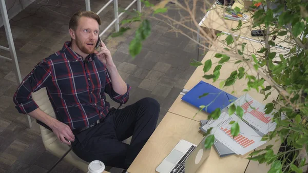 Навмисно бородатий чоловік сидить на стільці і розмовляє по телефону . — стокове фото