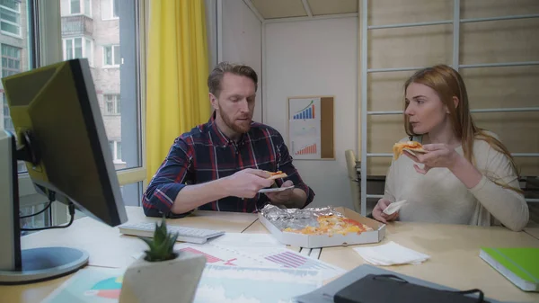 Hombre y mujer comiendo pizza en el lugar de trabajo . — Foto de Stock