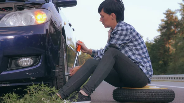 female changing a tire outdoors.