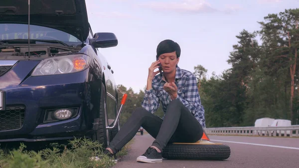 Motorista tentar mudar um pneu ao ar livre usando smartphone . — Fotografia de Stock