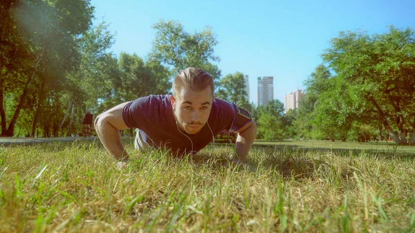 大胡子的小伙子正在推 ups 在草地上. — 图库照片