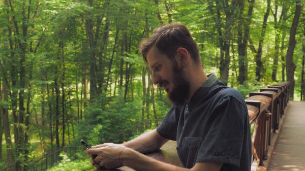 Un hombre guapo con un teléfono inteligente está mirando a la cámara y sm — Foto de Stock