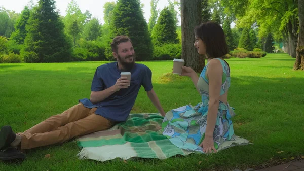 Le gars avec la fille assise dans le parc sur des couvertures sur la pelouse et boire du café . — Photo