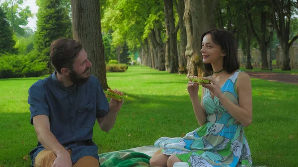 Jovem casal em um piquenique no parque segurando sanduíche . — Fotografia de Stock