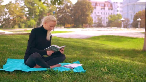 Szőke lány elolvassa a könyvet a parkban — Stock videók