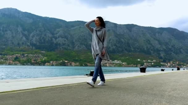 Femme d'âge moyen marchant par la côte près de l'eau. Montagnes sur fond — Video