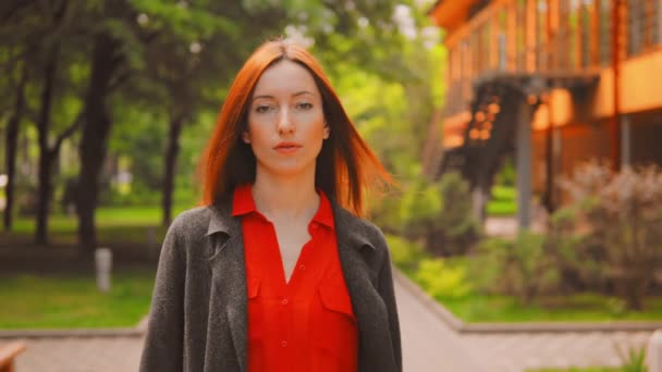 Fille aux cheveux rouges marchant dans un parc vert — Video