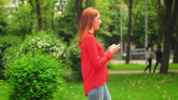 Meisje wandelen in groene zomer Park en sms'en berichten — Stockvideo