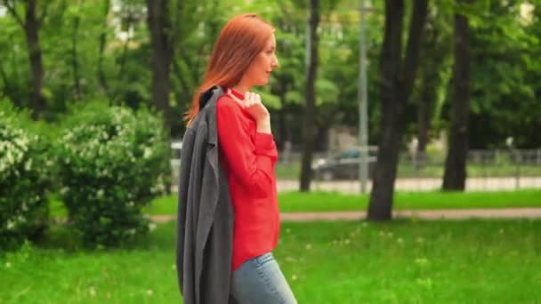 Red haired beauty walking in green park — Stock Video