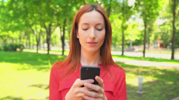 Jonge vrouw texting berichten in zomerpark — Stockvideo