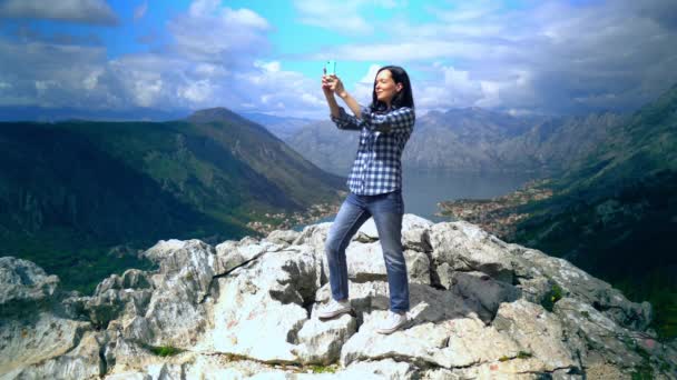 Жінка стоїть на вершині гори зі смартфоном і фотографує — стокове відео
