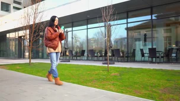 Pewna siebie kobieta Walking by ulica nowoczesnego miasta i patrząc na smartphone — Wideo stockowe