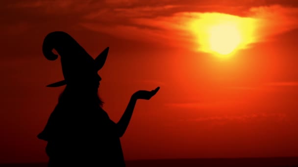 Ведьма дует на волшебный порошок на фоне восходящего солнца — стоковое видео