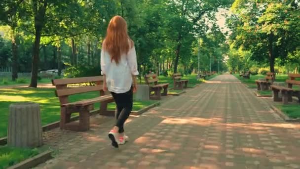 Женщина с рыжими волосами поворачивается к камере прогулки в весеннем городе — стоковое видео
