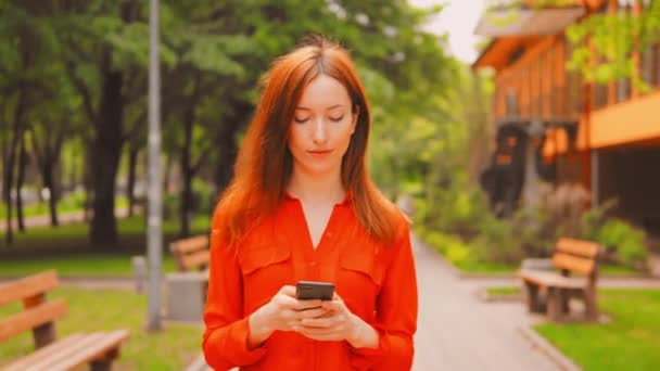 Redhead vrouw Scrolls touch screen op smartphone outdoor — Stockvideo