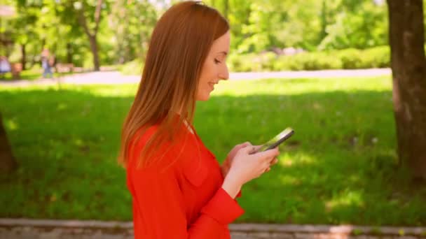 Side view redheaded businesswoman use mobile walks outdoors — Stock Video
