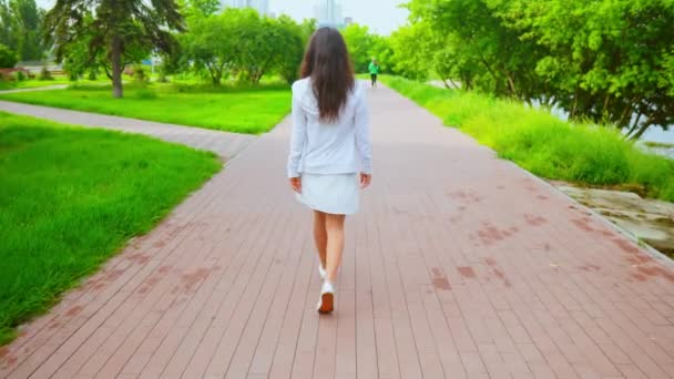Щаслива брюнетка гуляє в місті з зеленим літнім видом на природу — стокове відео