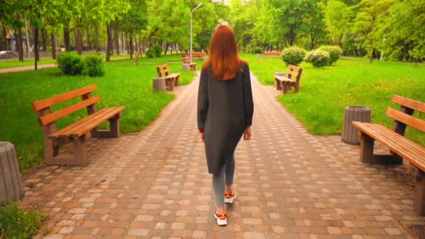 Onherkenbare vrouw met rood haar wandelingen in het park — Stockvideo