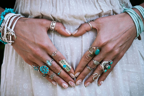 closeup of young woman hands in heart shape with lot of boho style jewrly, rings and bracelets outdoor summer day