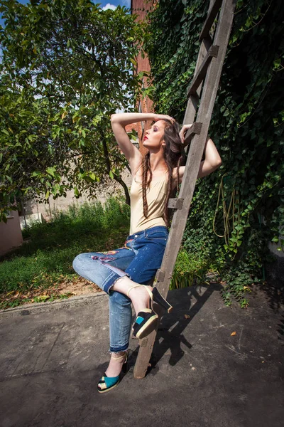 young woman in backyard summer fashion blue embroidered jeans and bodysuit-nude color and high heel sandals