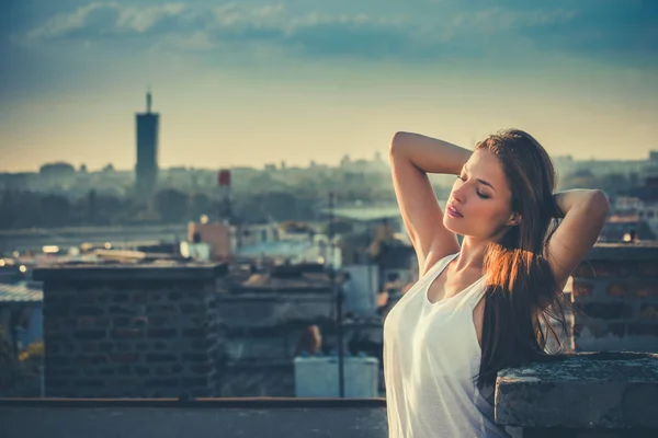 年轻美丽的城市女孩在白色顶部坦克享受在日落在屋顶夏天 — 图库照片