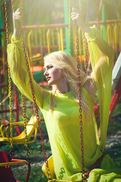長い黄色のドレスでカルーセルを飛んで遊園座っている美しい金髪のエレガントなファッション女性夏の日 — ストック写真