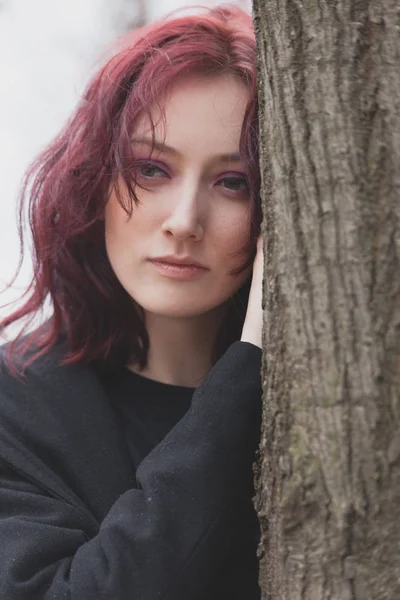portrait of young pale pensive  woman  lean on tree winter day in park closeup