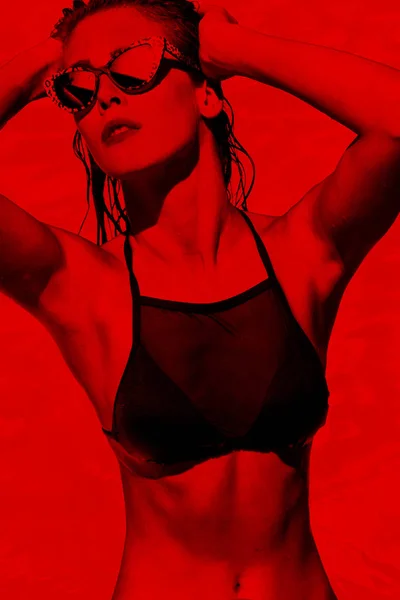 年轻迷人的女人在黑色比基尼和太阳镜在游泳池红色色调 — 图库照片