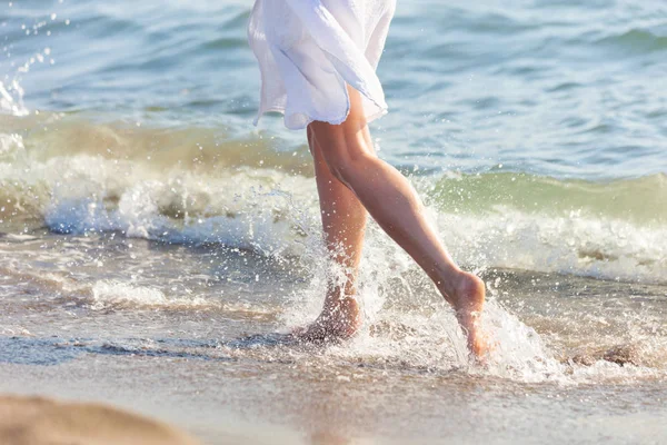 Mujer en vestido blanco correr a través del agua en la playa de arena del mar s —  Fotos de Stock