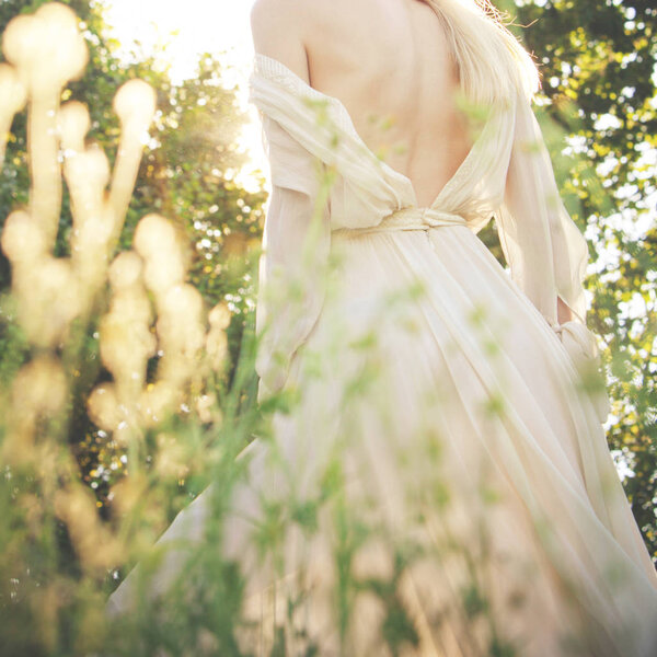 Young woman in elegant dress, bare back, summer day in field