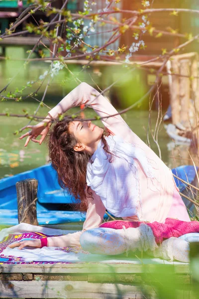 Молодая женщина практикует йогу на открытом воздухе весенний день у озера — стоковое фото